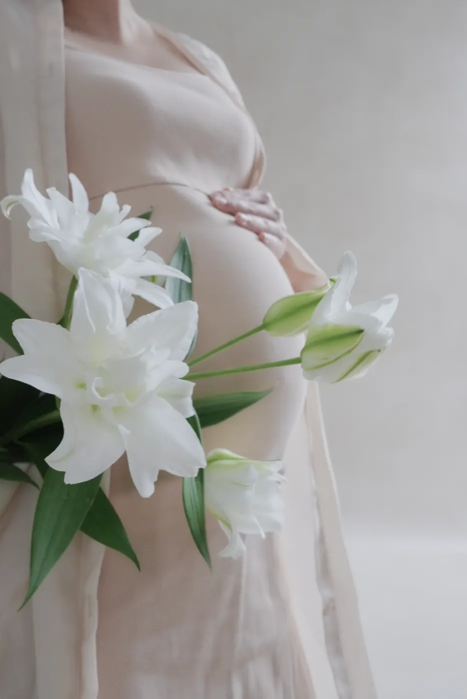 ベージュモルタル背景で百合の花を添えたマタニティフォトのクローズアップ