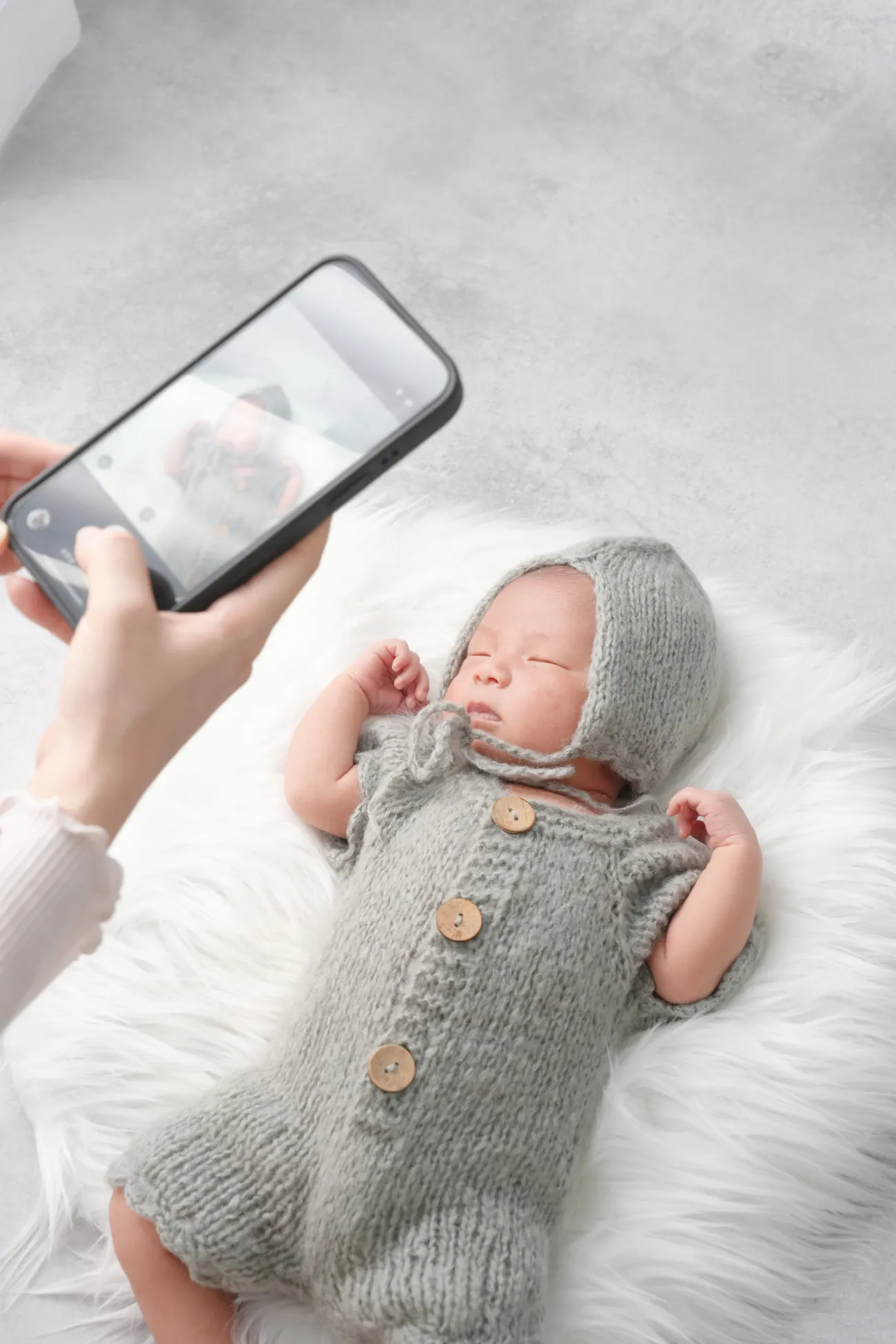 シートに寝かせた赤ちゃんをスマホで撮影している手元